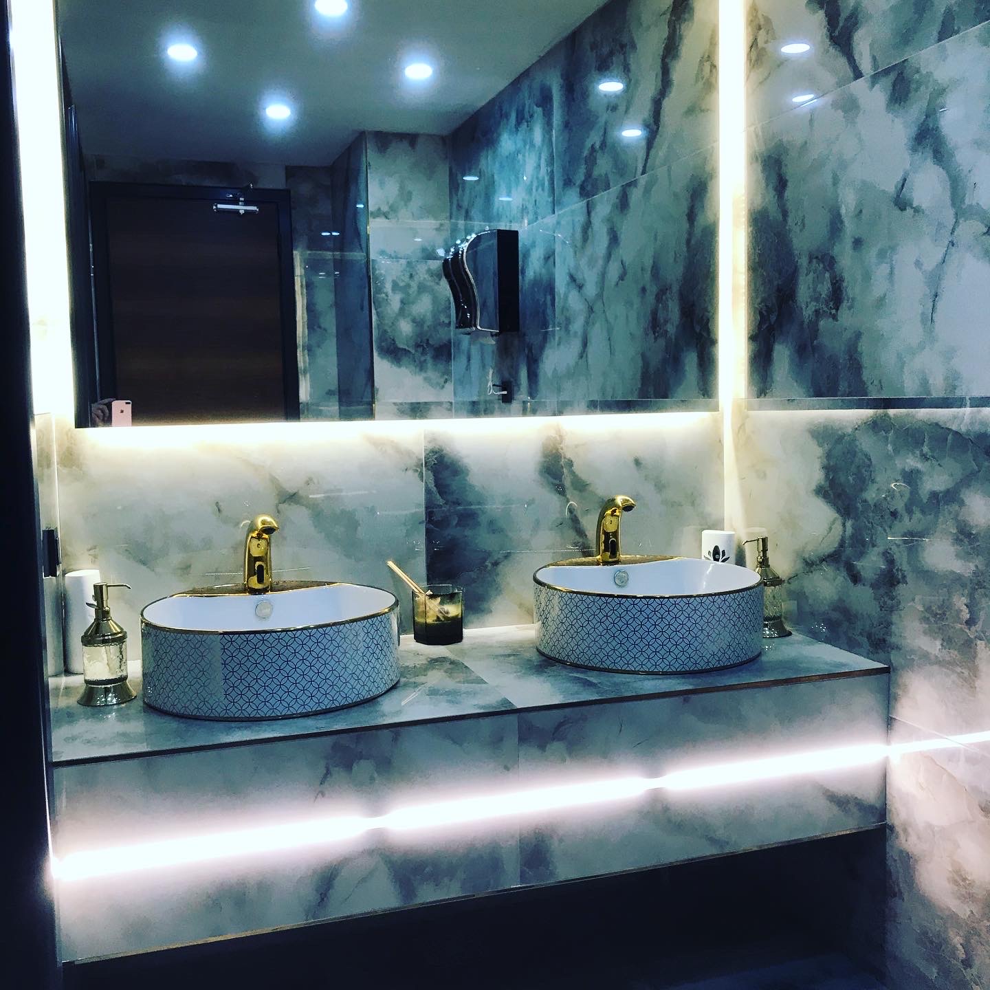 Backlit onyx powder room with patterned vessel basins and brass fittings.