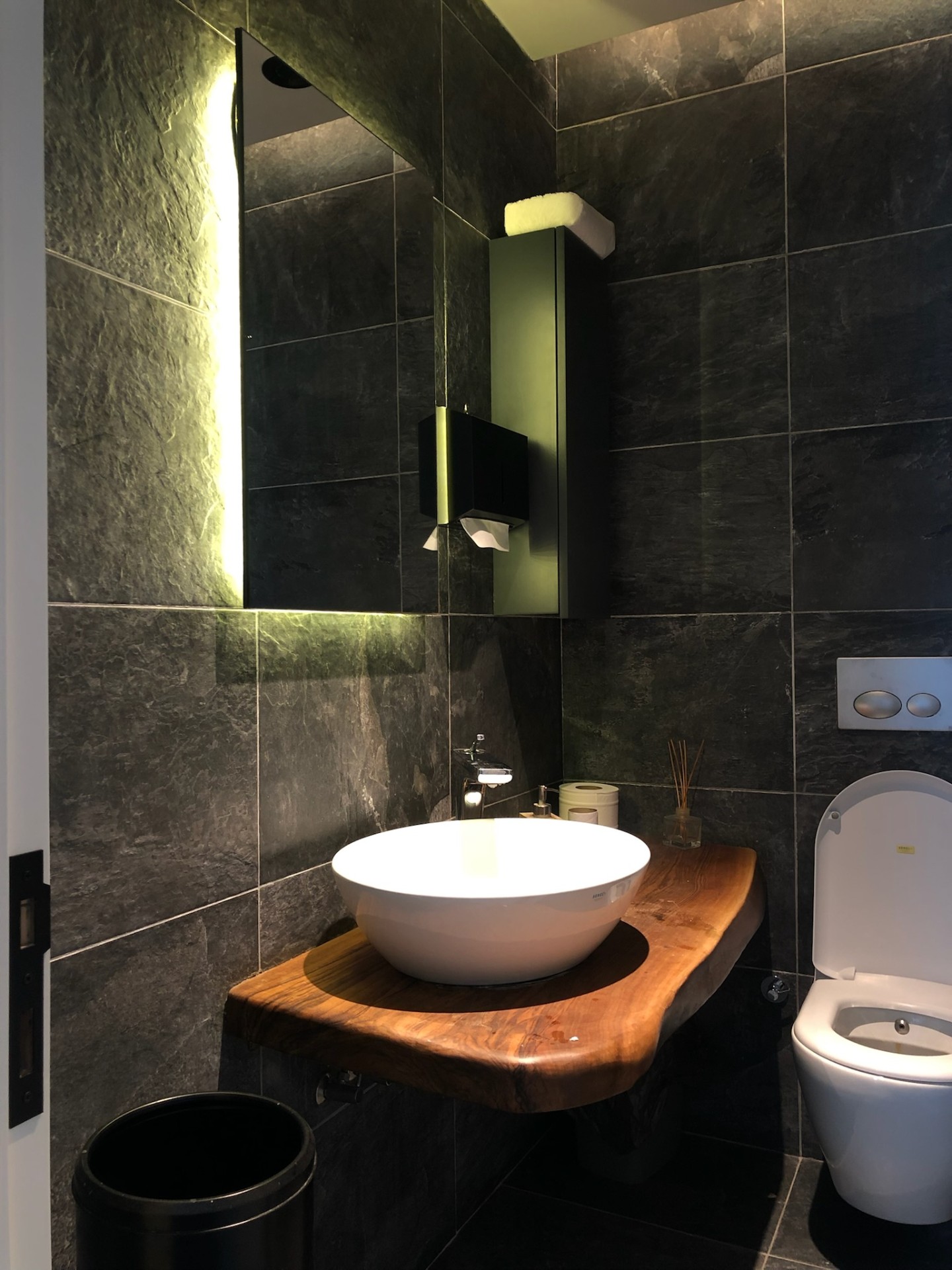Slate-tiled powder room with live-edge walnut slab shelf and floating white basin.