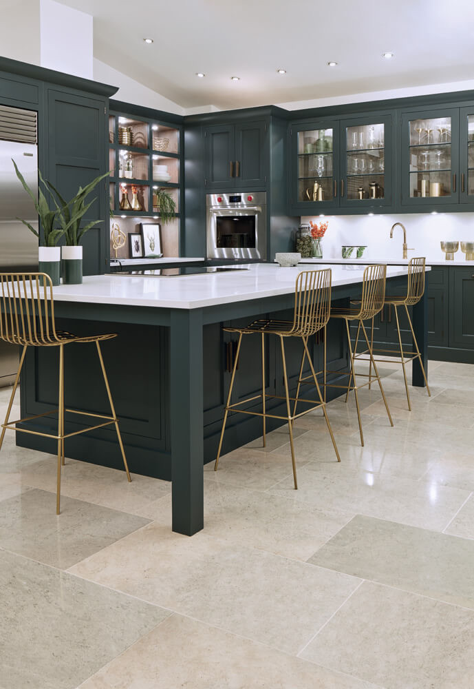 Forest green in-frame kitchen with brass bar stools and limestone floor