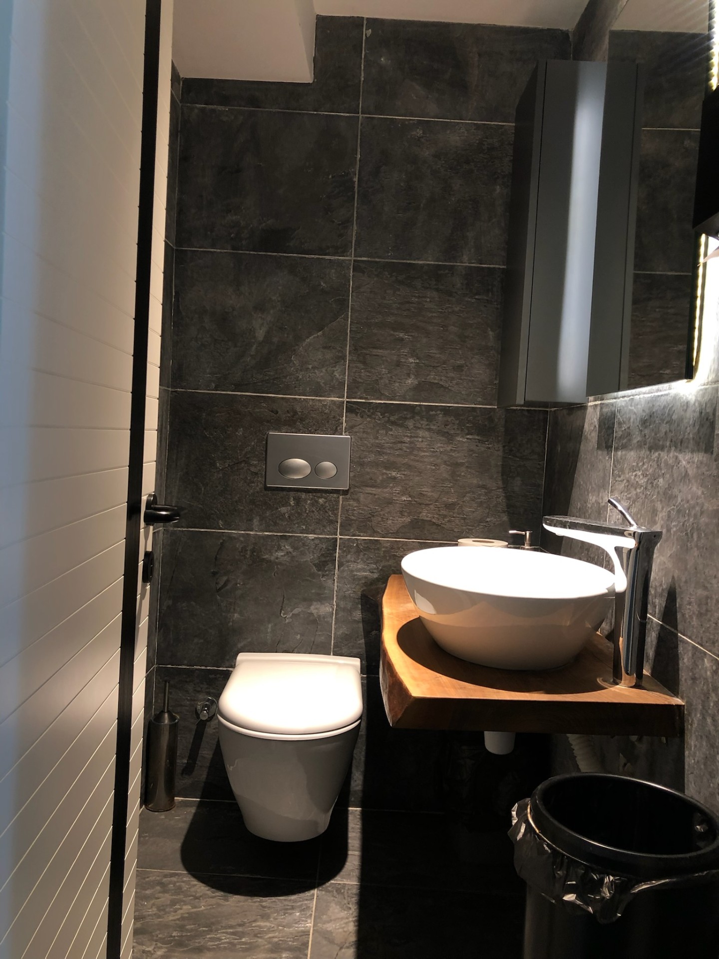 Compact commercial WC in slate with sculpted live-edge counter and floating storage.