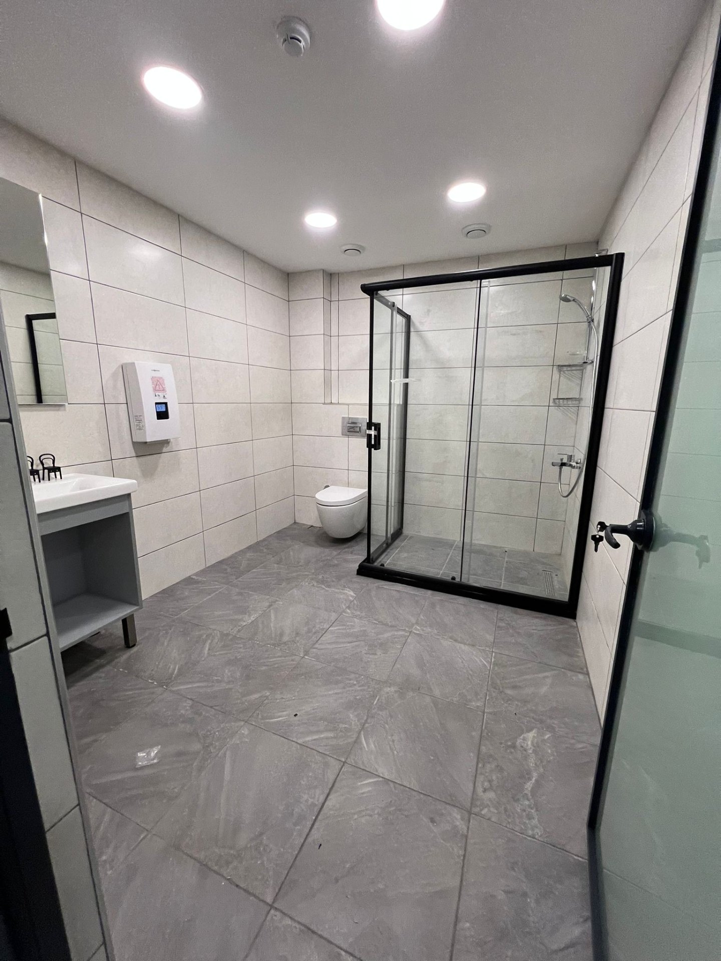 Contract-grade bathroom with black-framed shower and matte grey stone floor