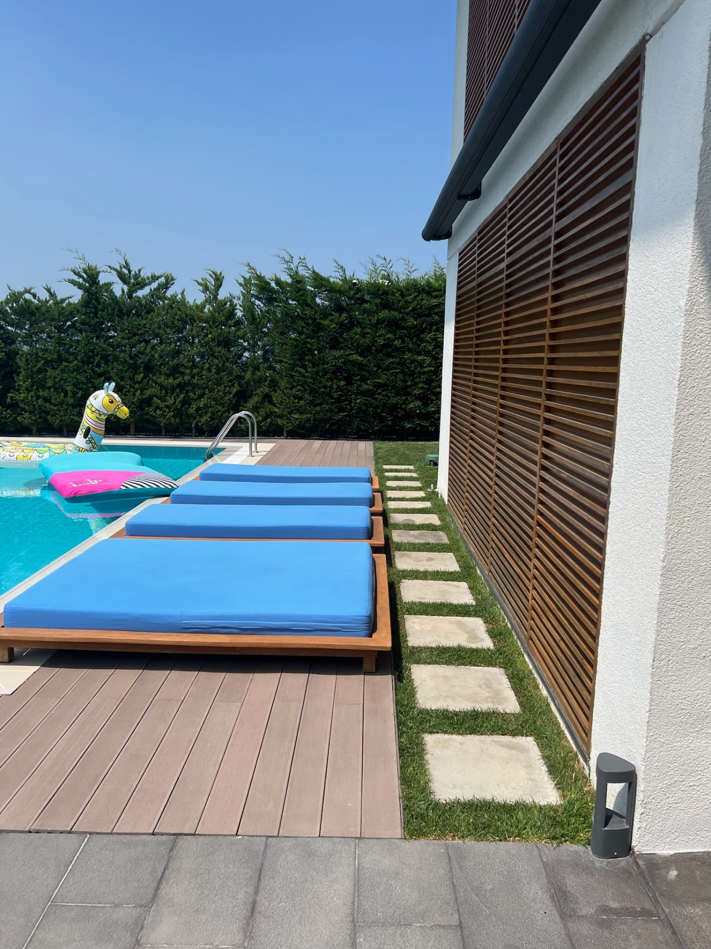 Slatted teak privacy façade with stepping-stone path and pool alignment.
