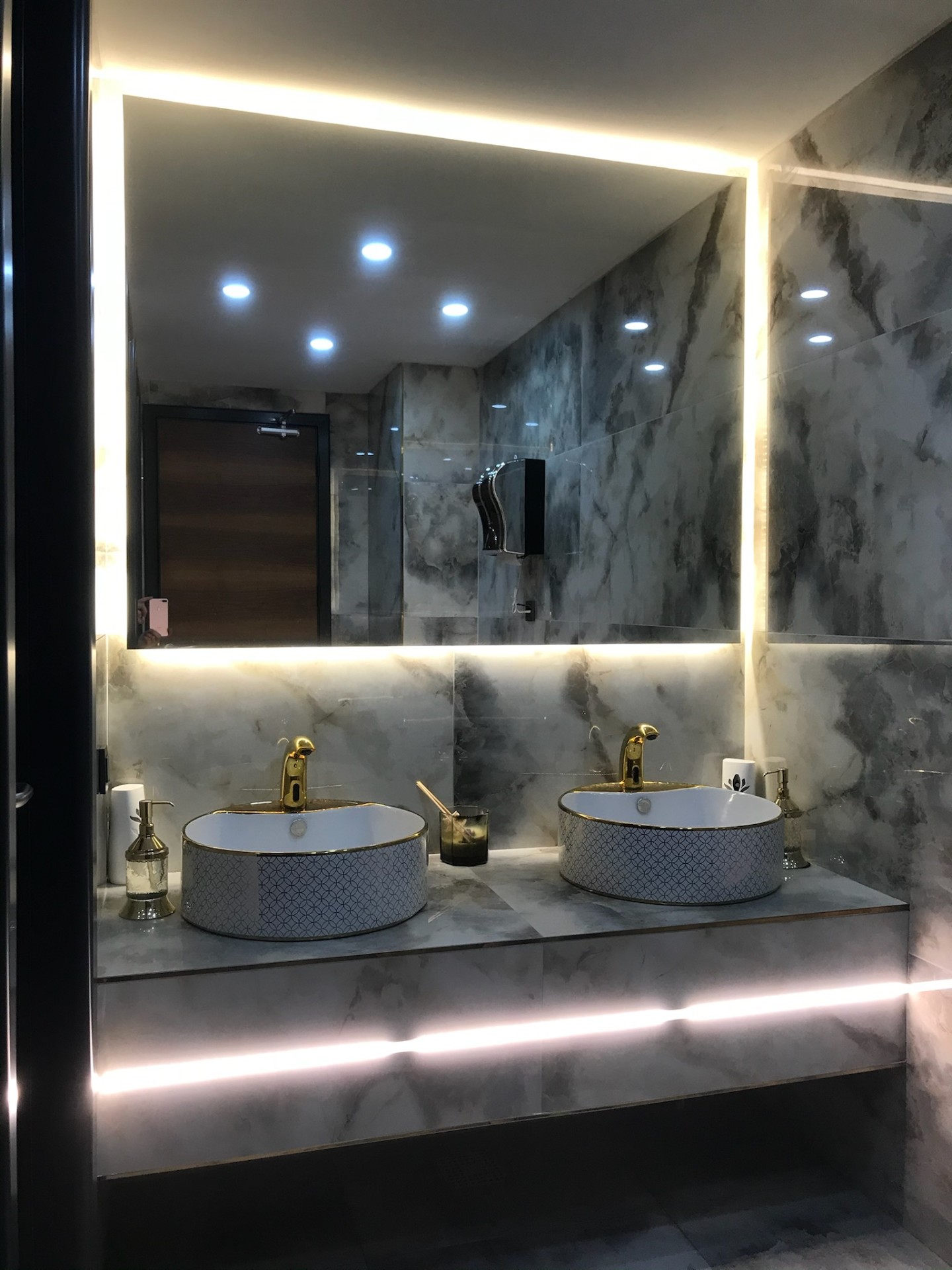 Grey onyx hospitality washroom with backlit LED mirror and patterned twin vessel basins.