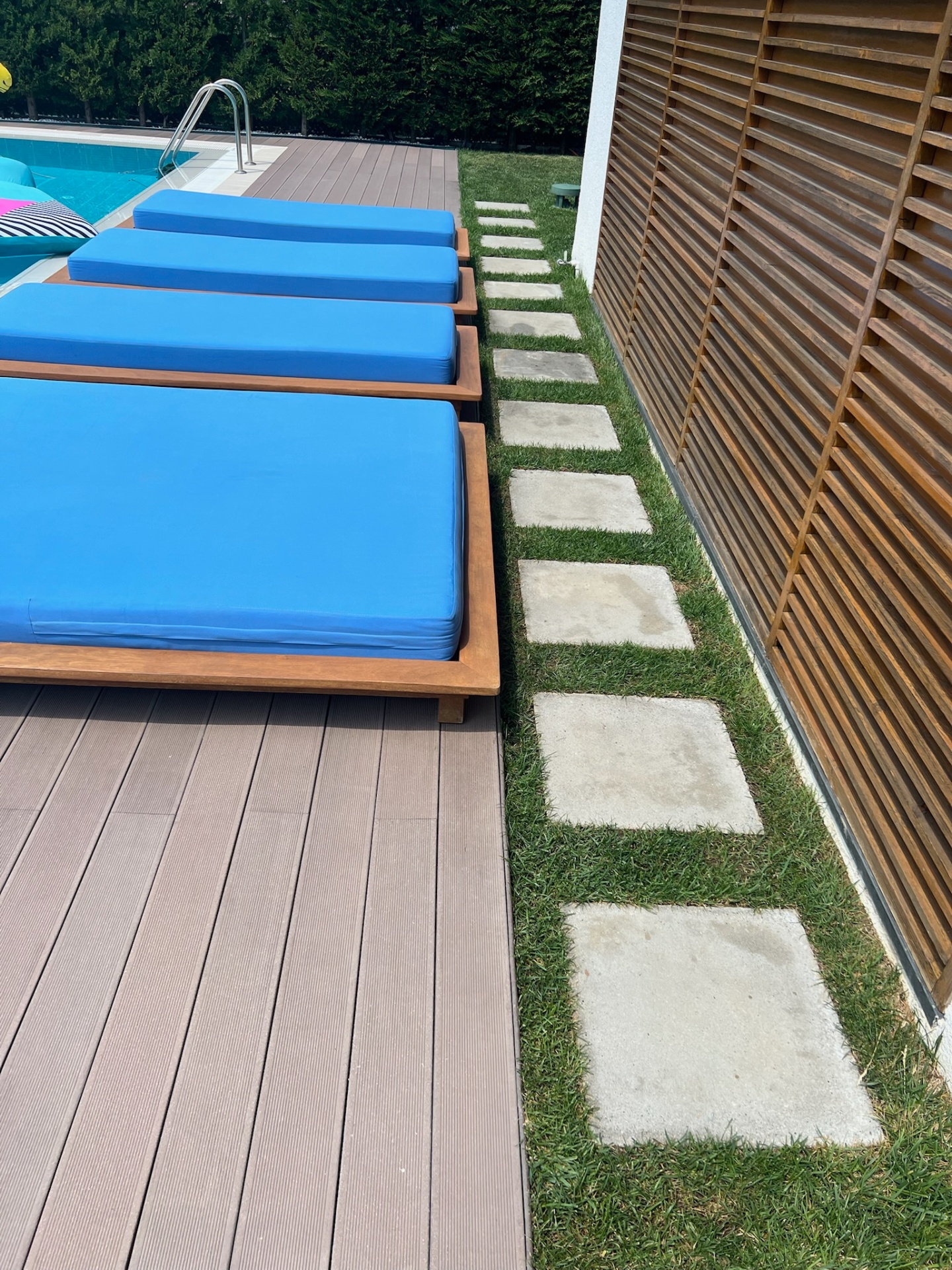 Detail — composite deck edge meets grass, stone and slatted teak wall.