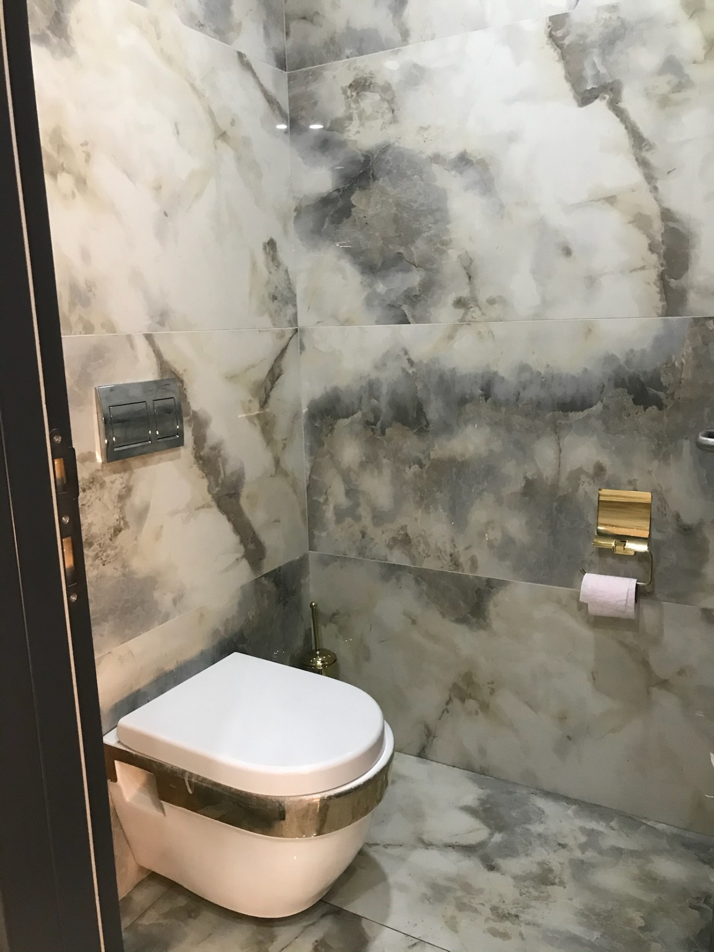 Book-matched grey onyx WC pod with brass hardware for a members-club suite.