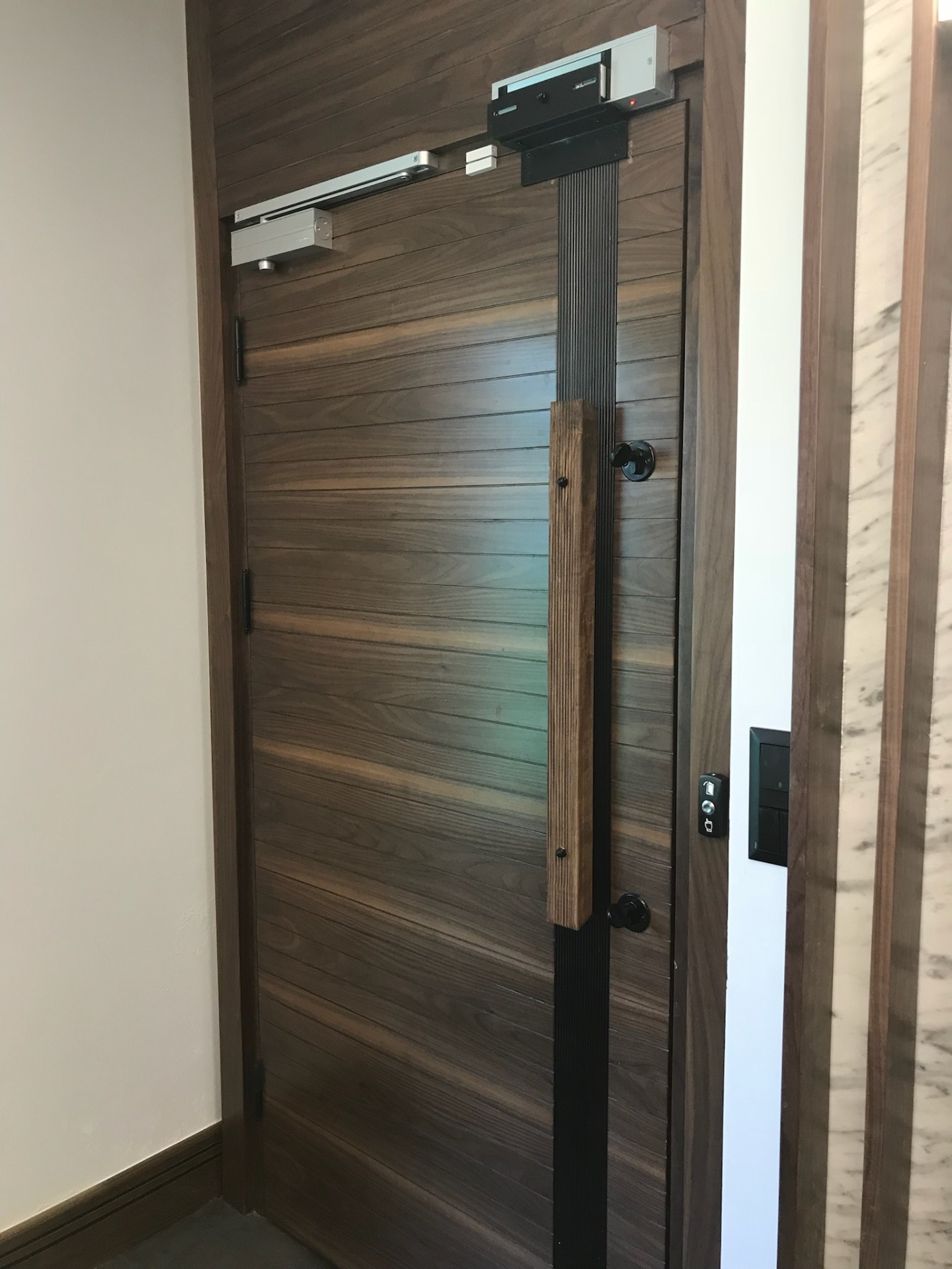 Horizontal walnut plank pivot door with concealed closer and fluted timber handle