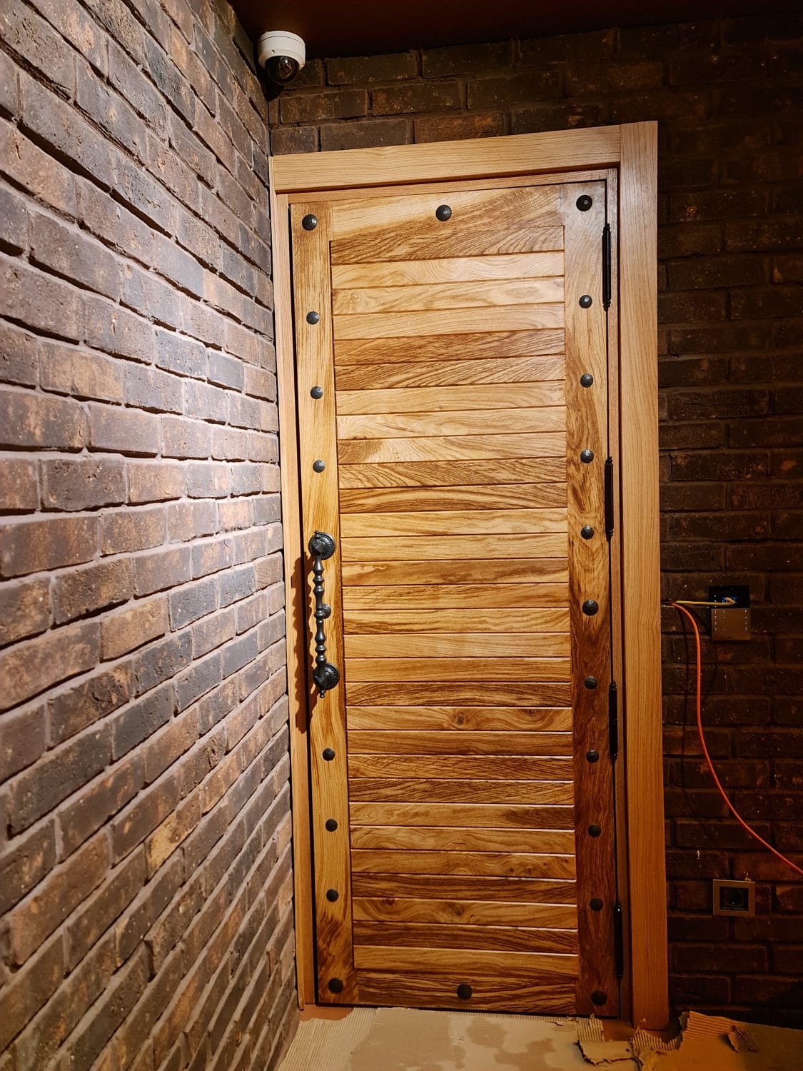 Horizontal oak plank door with hand-forged iron studs against reclaimed brick
