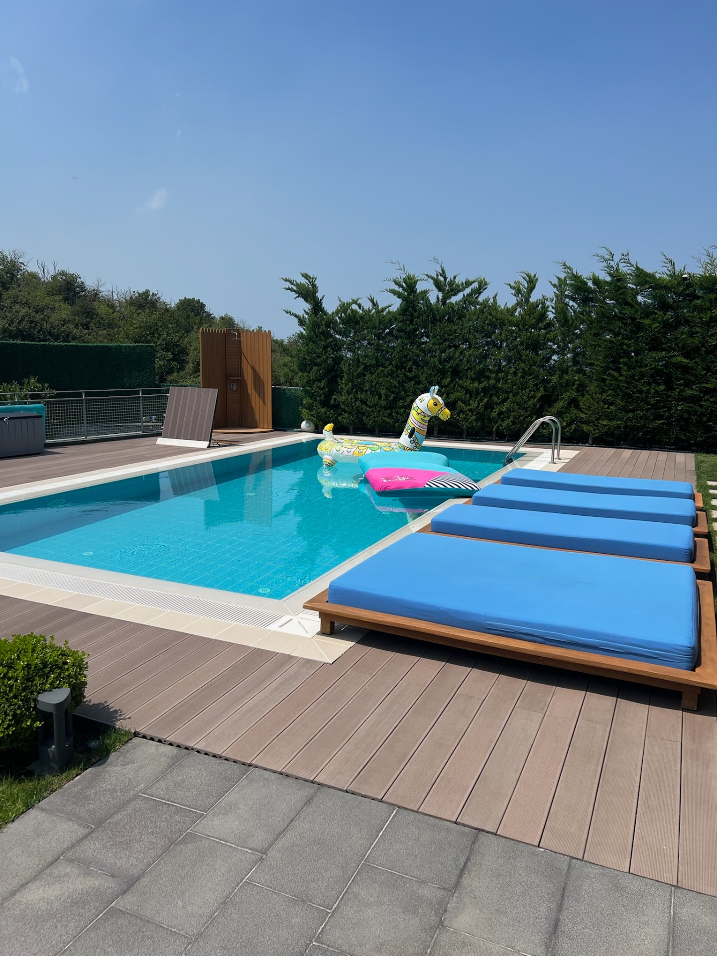 Poolside teak sun loungers on wide-plank composite deck.