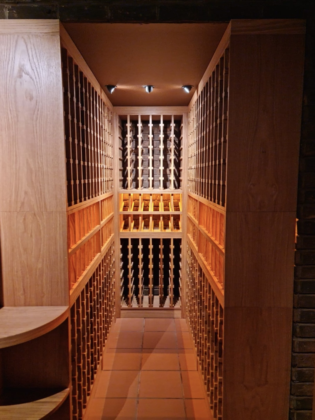 Backlit oak column racking framing a private cellar corridor.