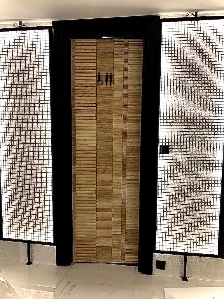 Sculpted timber block door framed by industrial mesh side lights