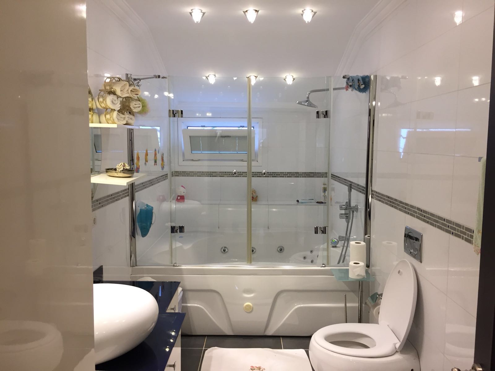 Chrome & glass ensuite — whirlpool bath framed by chrome-hinged screens under jewel-cut lighting.